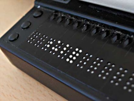 Monitor brajlowski: ma trzy przycisku po lewej stronie, które służą do pisania alfabetem Braille'a, oraz kilka rzędów pośrodku wysuwających się i chowających pręcików służących do wyświetlania tekstu.